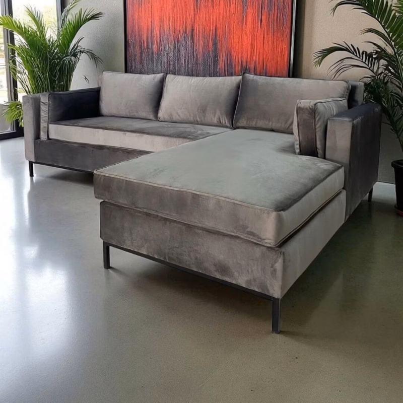Modern grey velvet L-shape couch with a wide chaise, styled with indoor plants and abstract wall art